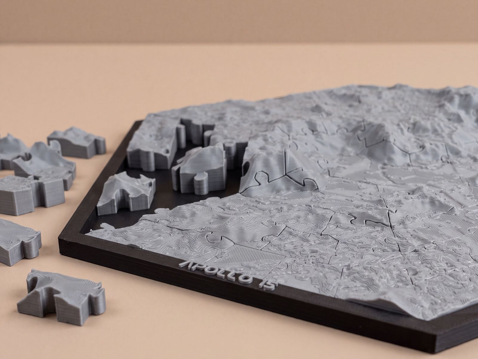An Apollo 15 terrain jigsaw puzzle printed in gray, with loose pieces beside its black frame